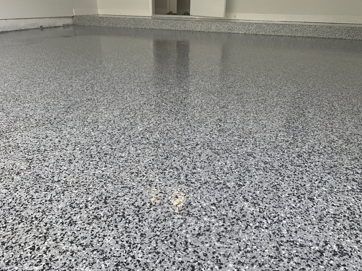 Black, white and grey epoxy flake garage floor with a glossy finish and matching flake cove base
