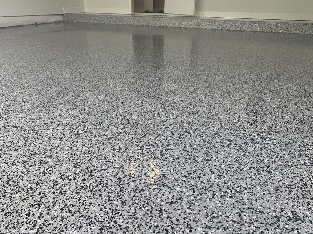 Black, white and grey epoxy flake garage floor with a glossy finish and matching flake cove base